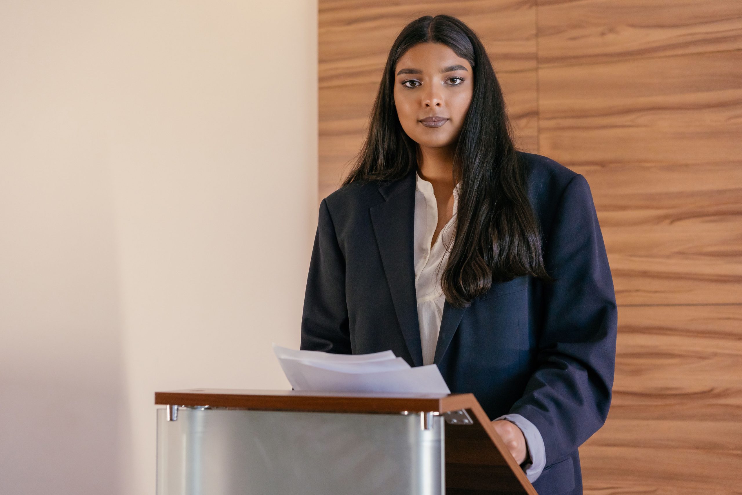 Confident woman in a suit speaking at a podium, representing a charismatic figure claiming to champion a cause