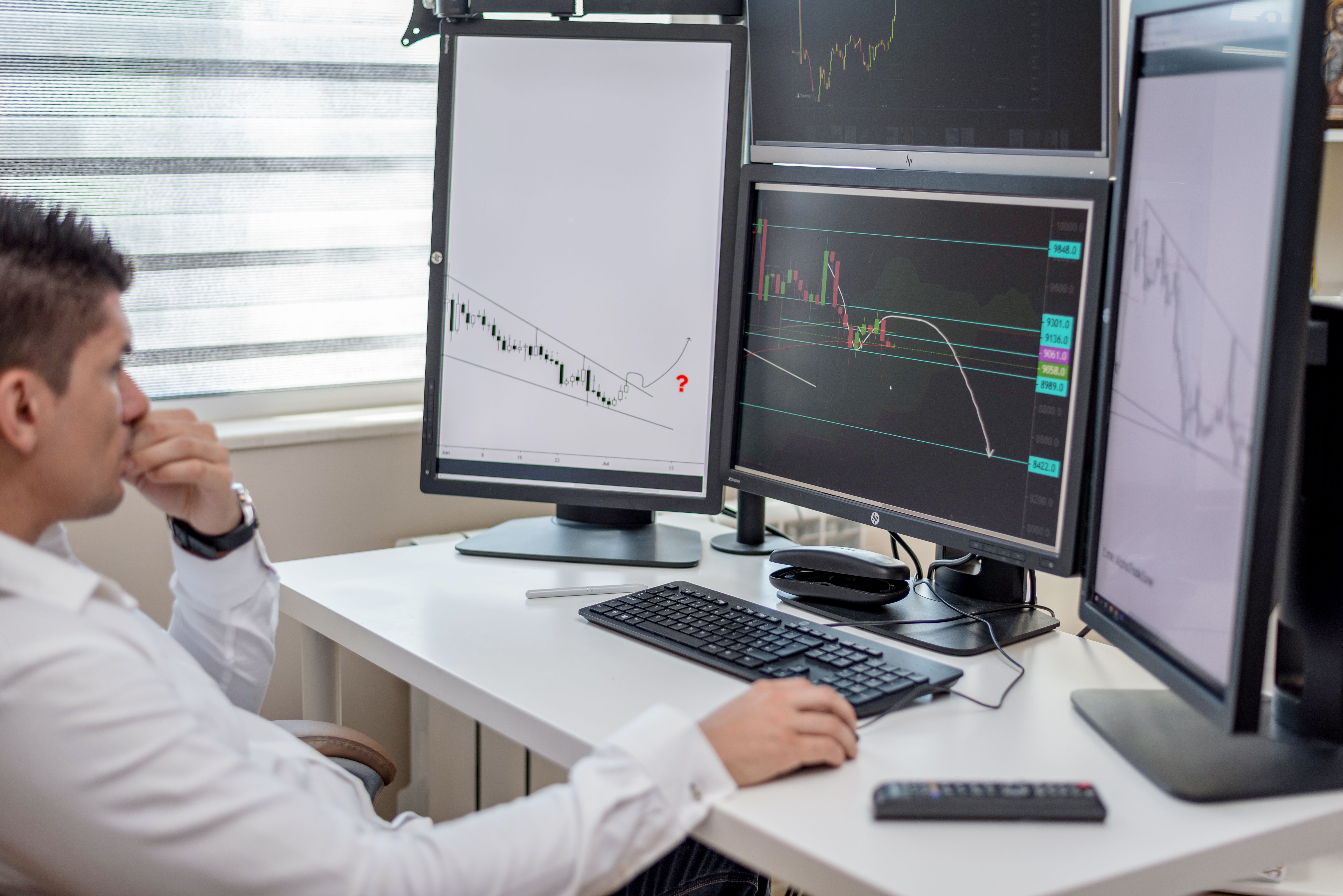 Business professional analyzing financial data on multiple monitors, assessing litigation investment risk