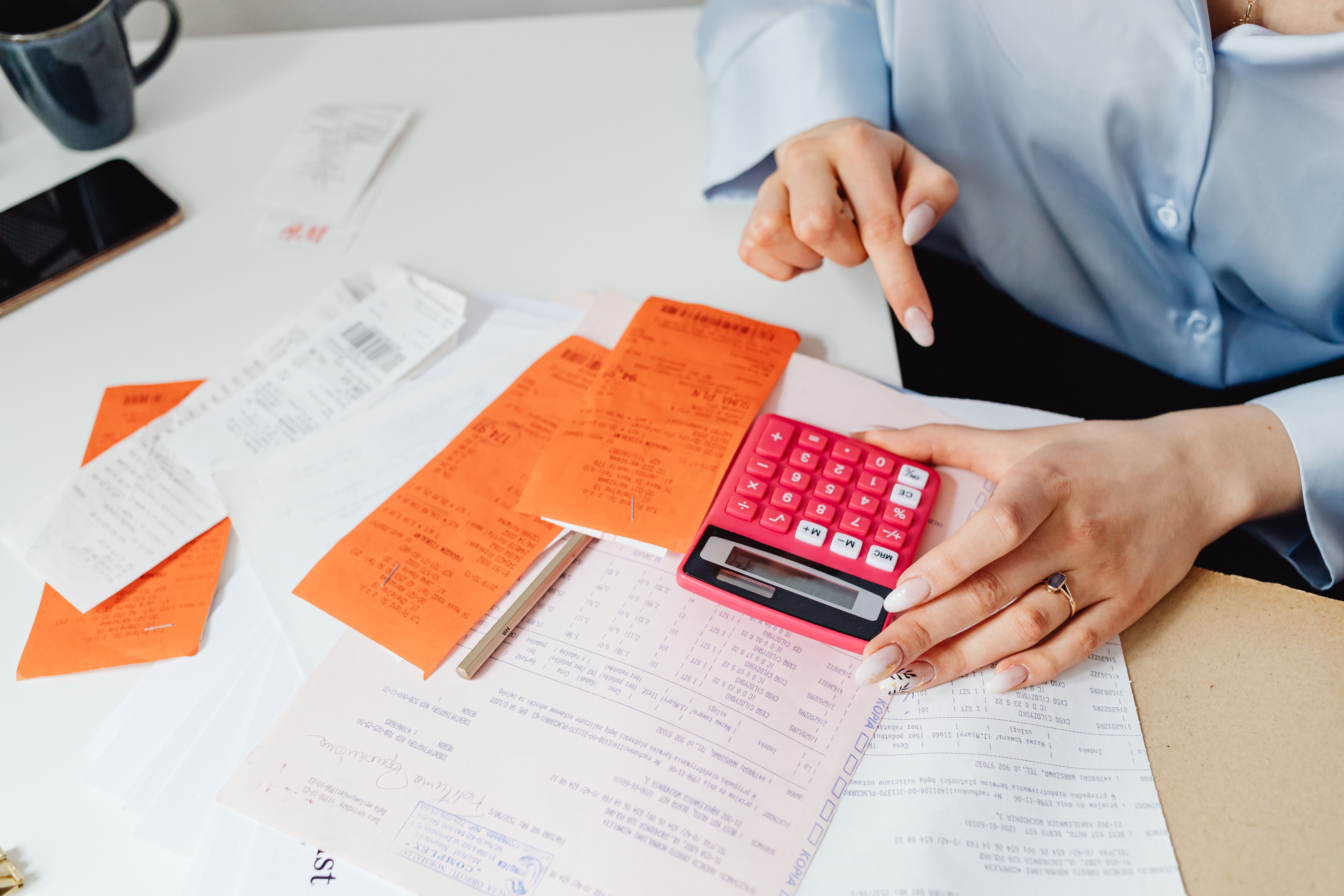 Businesswoman calculates expenses using receipts and calculator at desk.