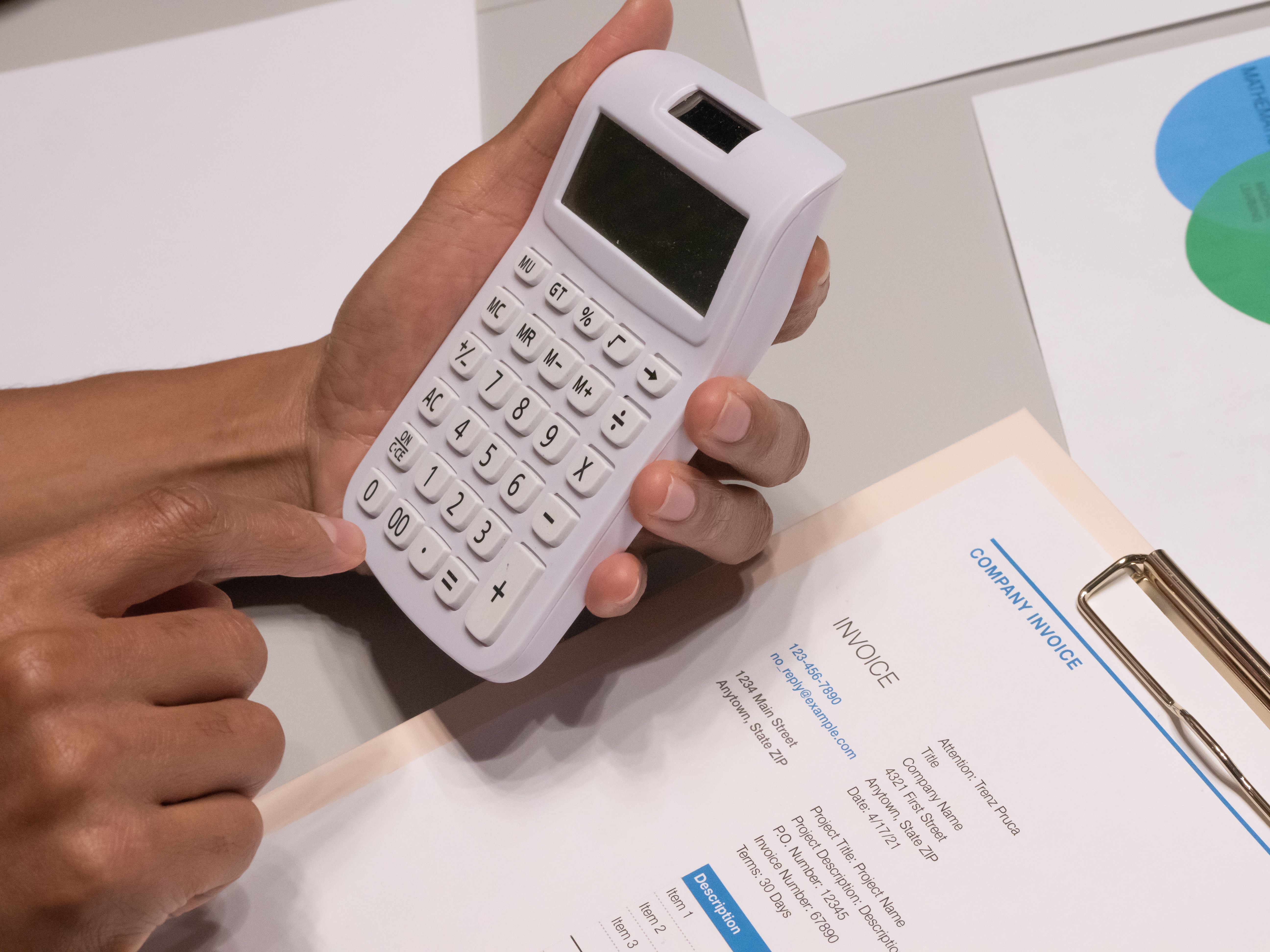 Close-up of hands using a calculator next to a company invoice.